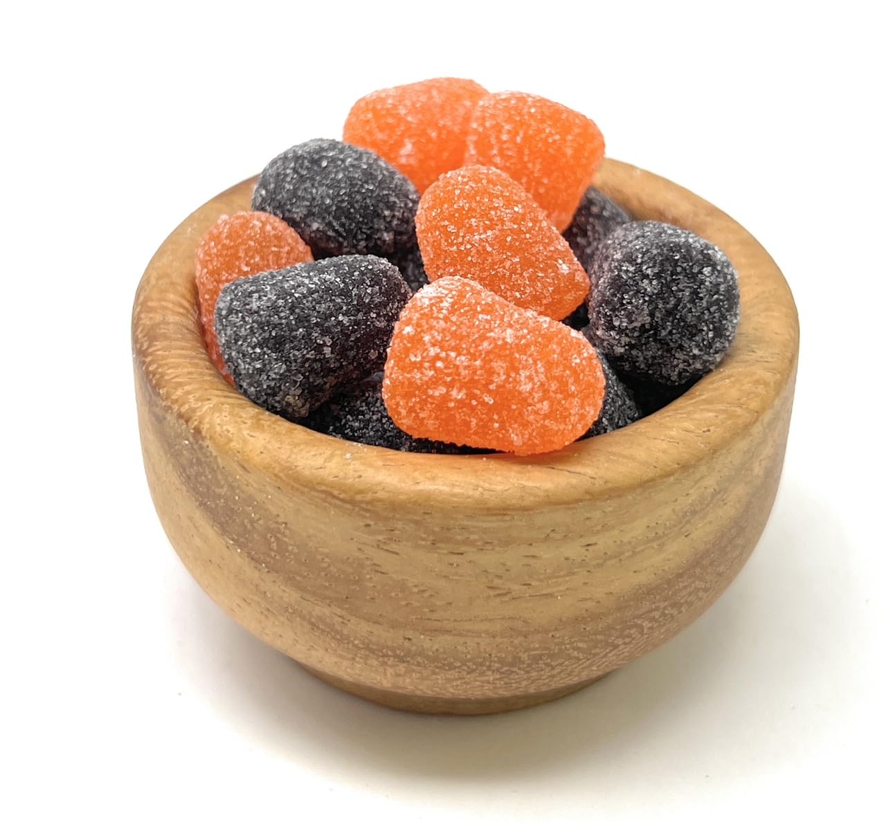 Wooden bowl filled with orange and black licorice spice drop candies on a white background