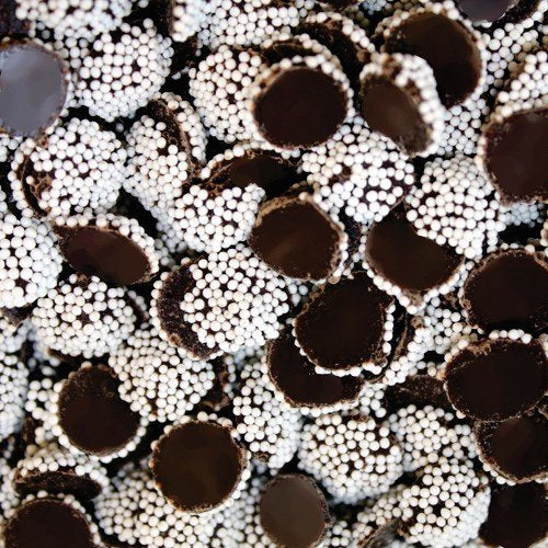 A close-up image of miniature dark chocolate drops with white nonpareil candies distributed throughout.