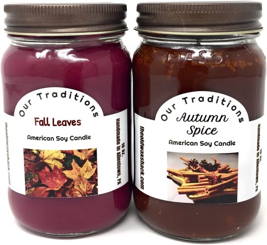Two soy candles, one labeled 'Fall Leaves' with a burgundy label and leaf images, and the other labeled 'Autumn Spice' with a brown label and cinnamon sticks images.
