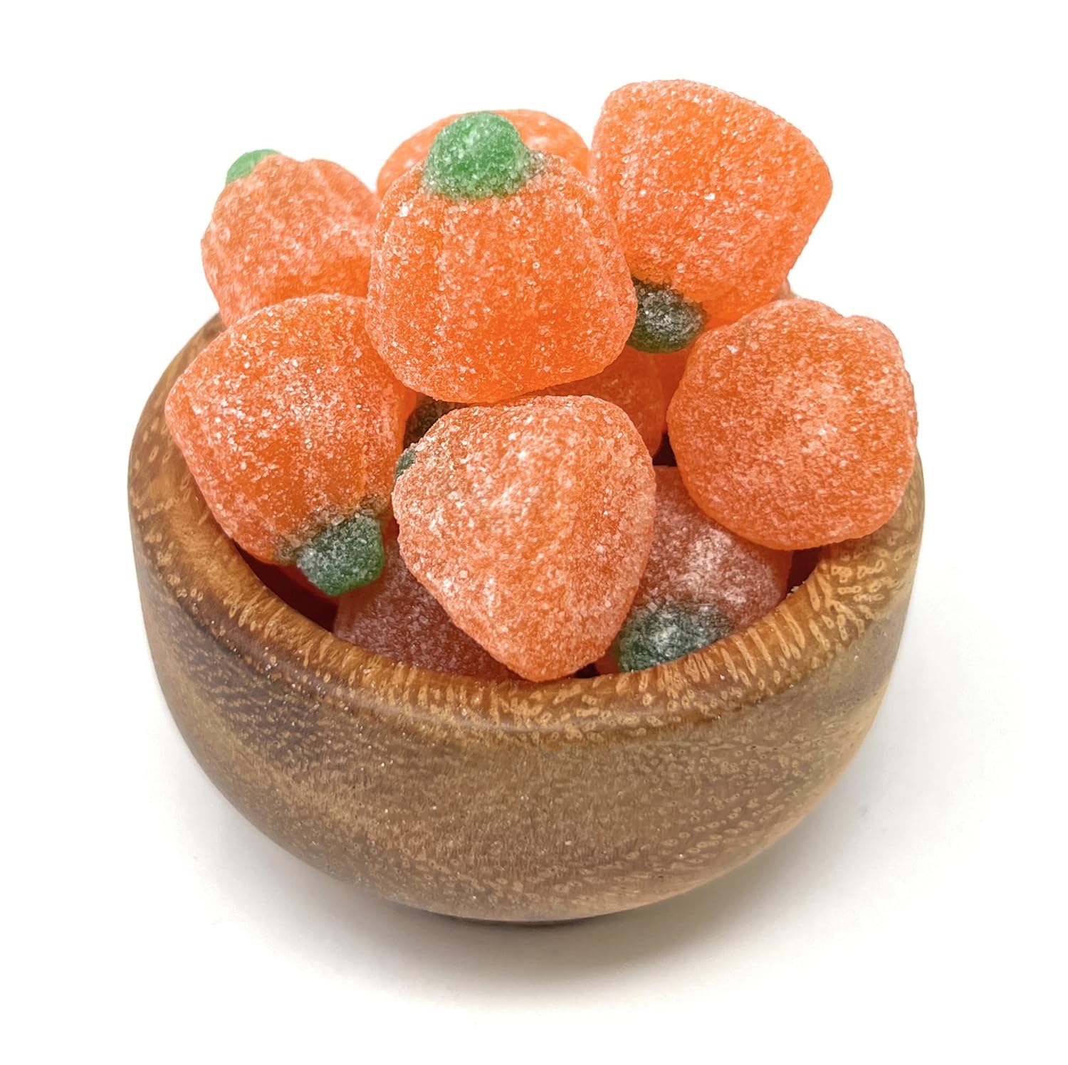 Wooden bowl filled with orange jelly pumpkins on a white background