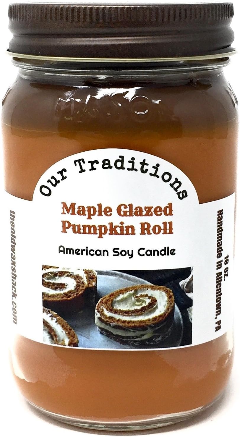 A 16 oz jar candle with a dark brown lid and a white label reading 'Our Traditions Maple Glazed Pumpkin Roll American Soy Candle'. The candle wax inside is a warm pumpkin spice color, and the label shows photos of pumpkin roll slices.