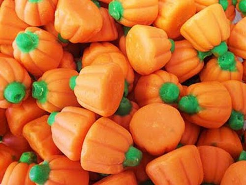 A close-up image of small, orange-Mello creme pumpkin candies shaped like pumpkins with green accents on the stem.