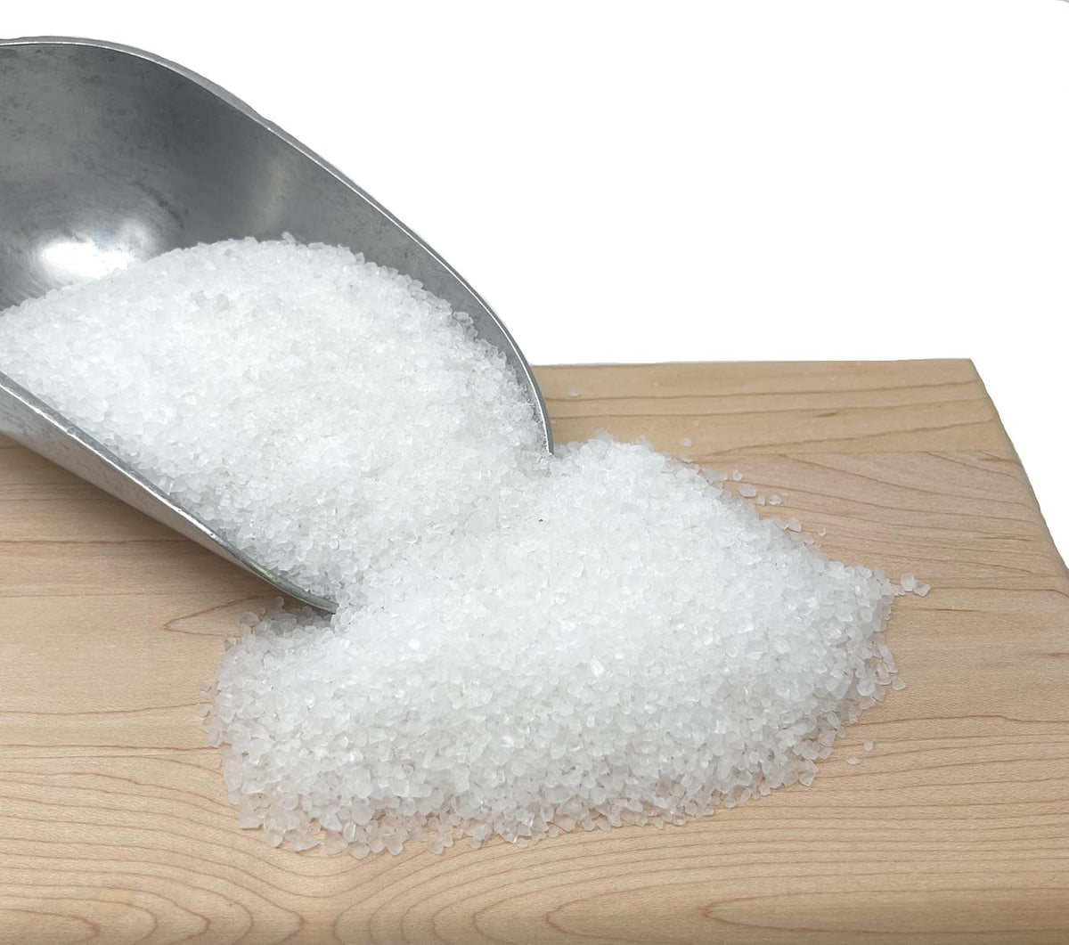 White coarse sea salt on a wooden surface with a metal scoop.