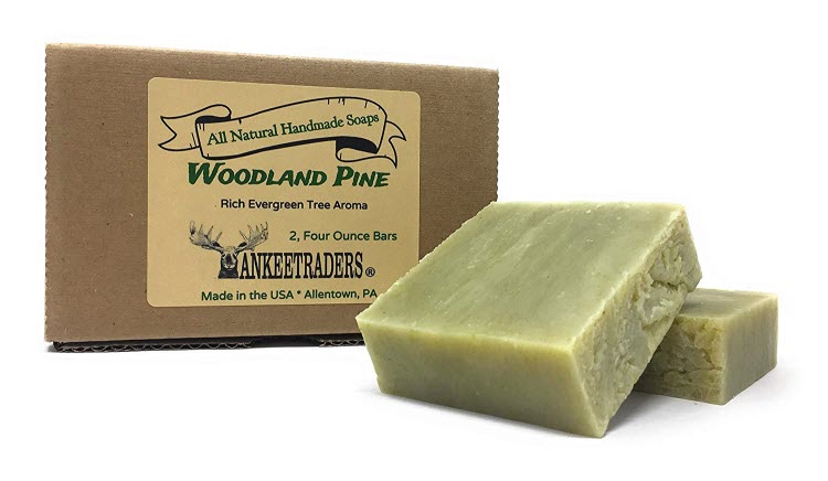 Two bars of handmade, all natural vegan soap with a greenish tint, accompanied by its packaging which reads 'Woodland Pine All Natural Handmade Soap 2 - 4 Oz Bars'.